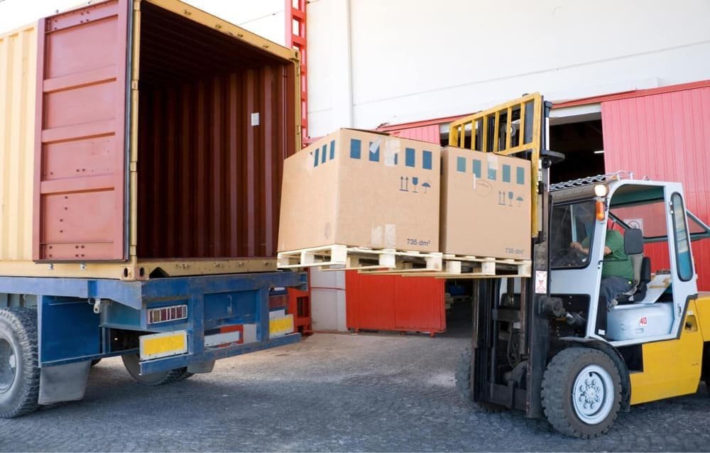 A forklift loads cardboard boxes onto a shipping container truck