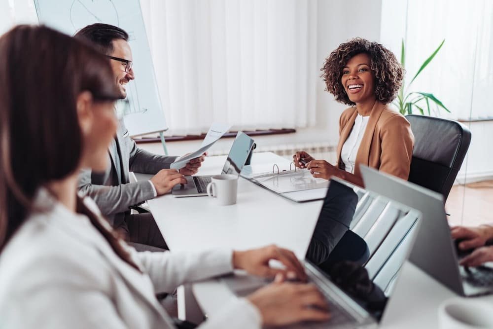 People having a meeting at a conference table, focusing on a smiling woman with curly hair