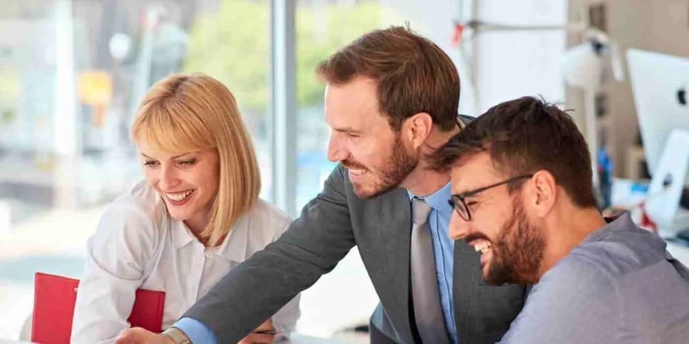 Three people seated together in an office, smiling and looking at a computer screen