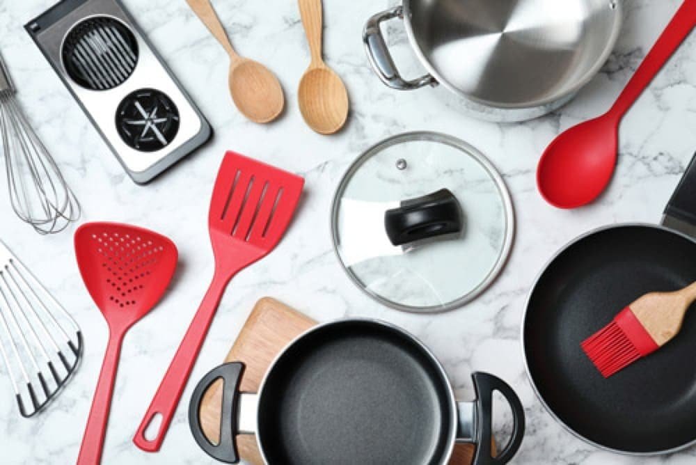 A variety of kitchen utensils and cookware on a marble surface, featuring red utensils and metal pots