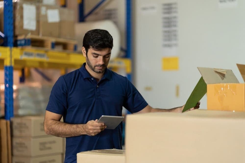 A man in a warehouse using a tablet among shelves and boxes