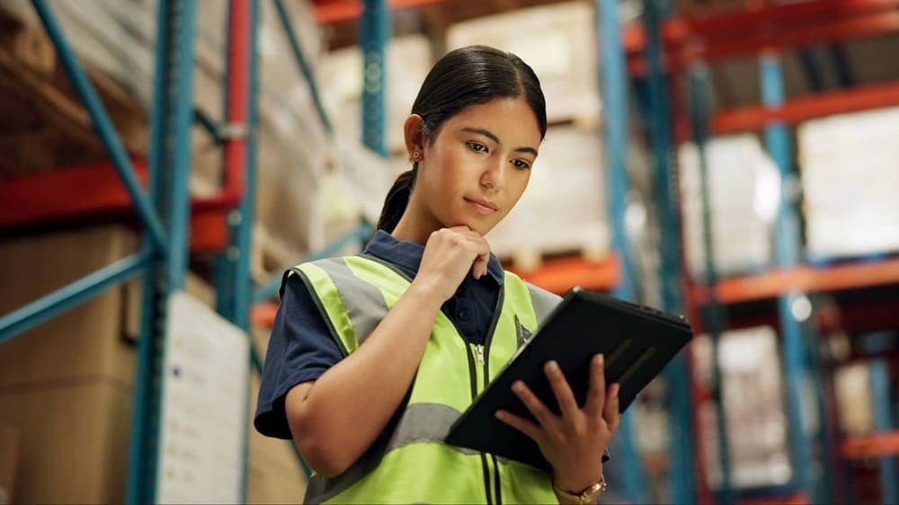 Person in a high-visibility vest holding a tablet in a warehouse