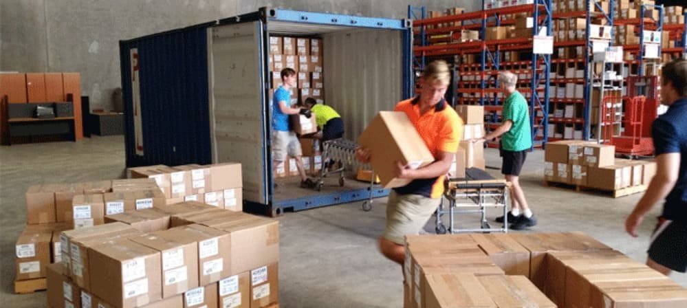 People unloading boxes from a shipping container in a warehouse