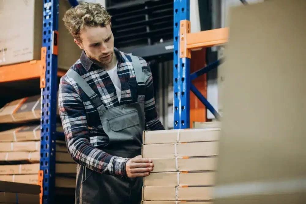 Person stacking boxes in a warehouse with blue and orange shelving