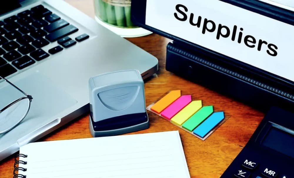 Office desk with laptop, stamp, calculator, sticky notes, and "Suppliers" binder