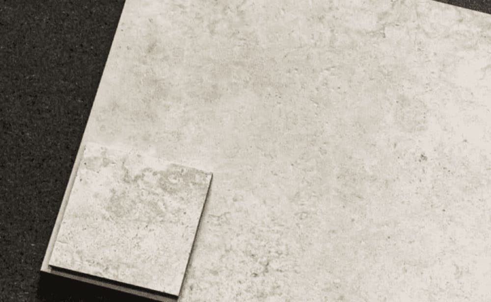 Two beige stone tiles on a dark textured surface; one large rectangular tile with a smaller square tile on top