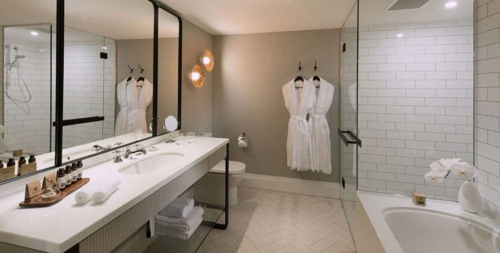 Modern bathroom with white countertop, glass shower, hanging bathrobes, and a tub