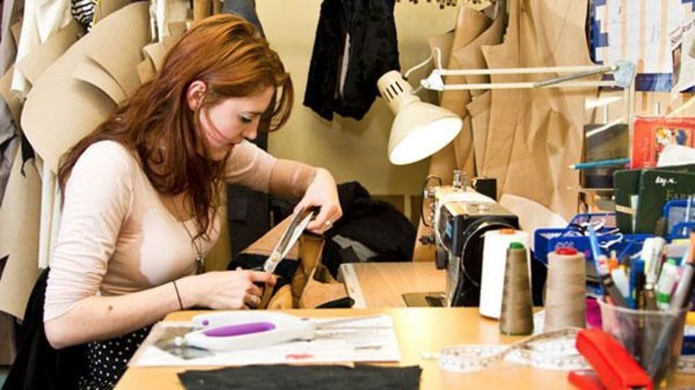 Woman sewing fabric at cluttered workstation with sewing machine and tools