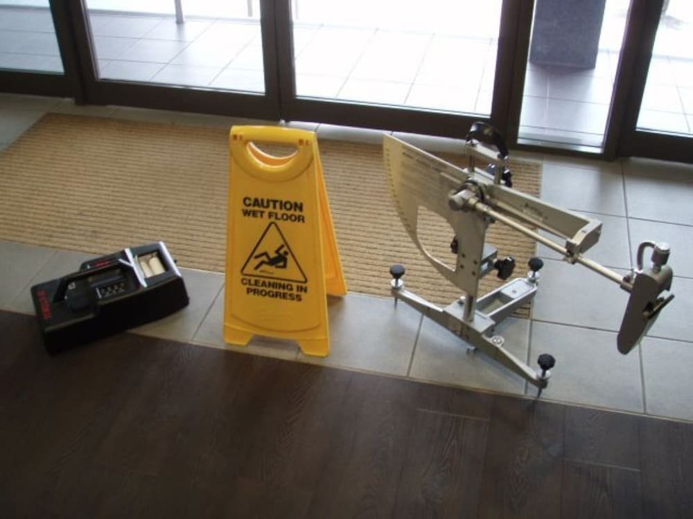 A wet floor sign between a black device and a silver mechanical instrument on mixed flooring