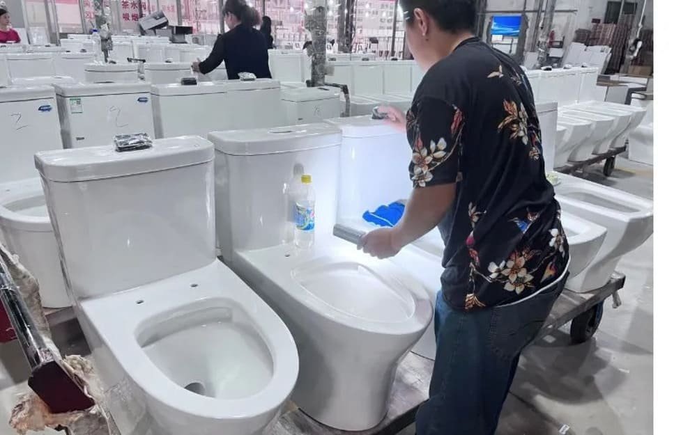 Person inspecting a row of white ceramic toilets in a manufacturing setting