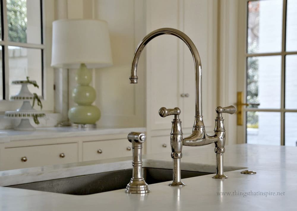 Modern kitchen sink with a curved metal faucet, white cabinetry, and a green lamp