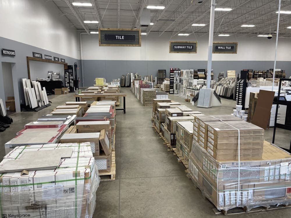 Interior of a large store with rows of tile pallets and overhead signs for different tile sections