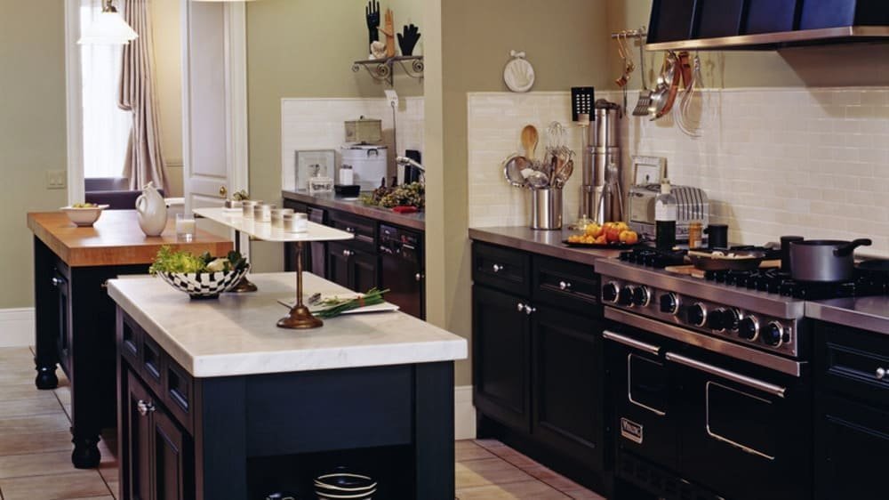Dark kitchen with marble countertops, stove with pots, hanging utensils, and fruit bowl