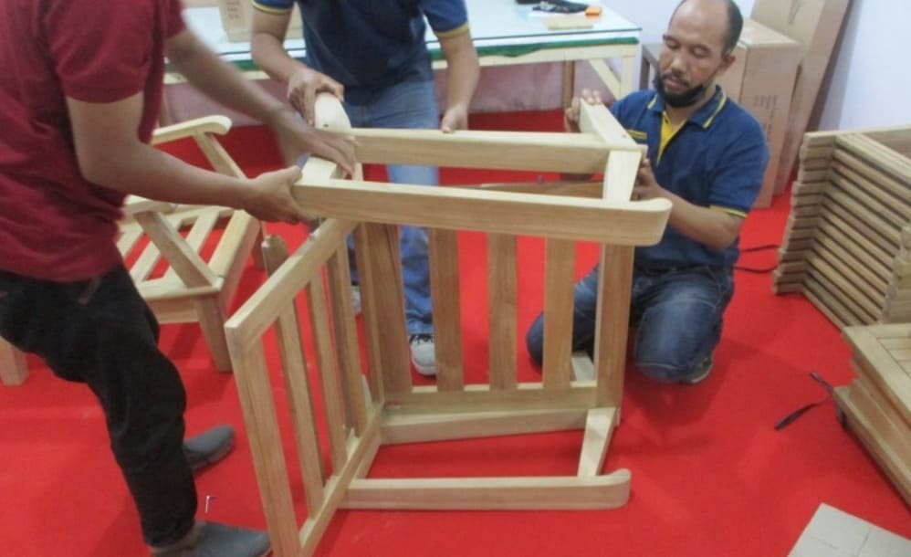Two people assembling a wooden chair during production on a bright red carpet