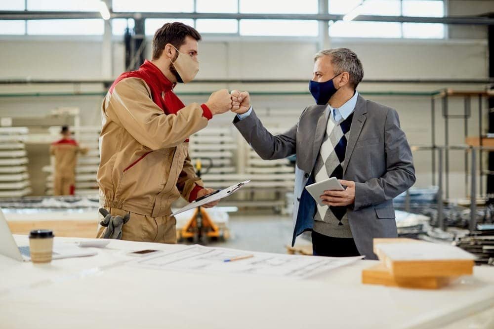 Furniture quality control team fist bump in a manufacturing facility wearing face masks
