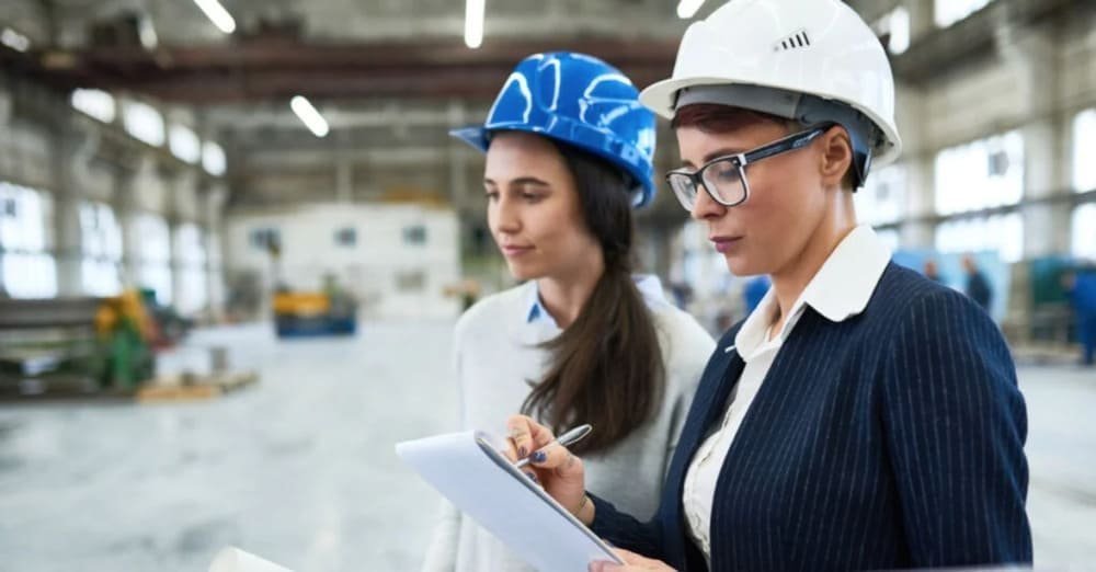 Two women in hard hats inspecting factory floor and taking notes